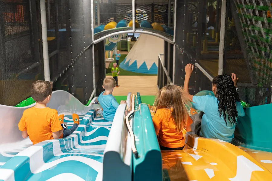Four kids racing down the big Funrise slide toward the mountain mural